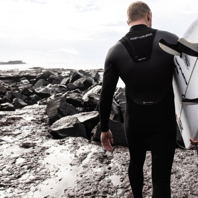 Surfista con neopreno poniéndose un guante junto al mar