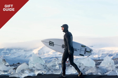 Surfer in a winter wetsuit and hood carrying a surfboard across the dunes