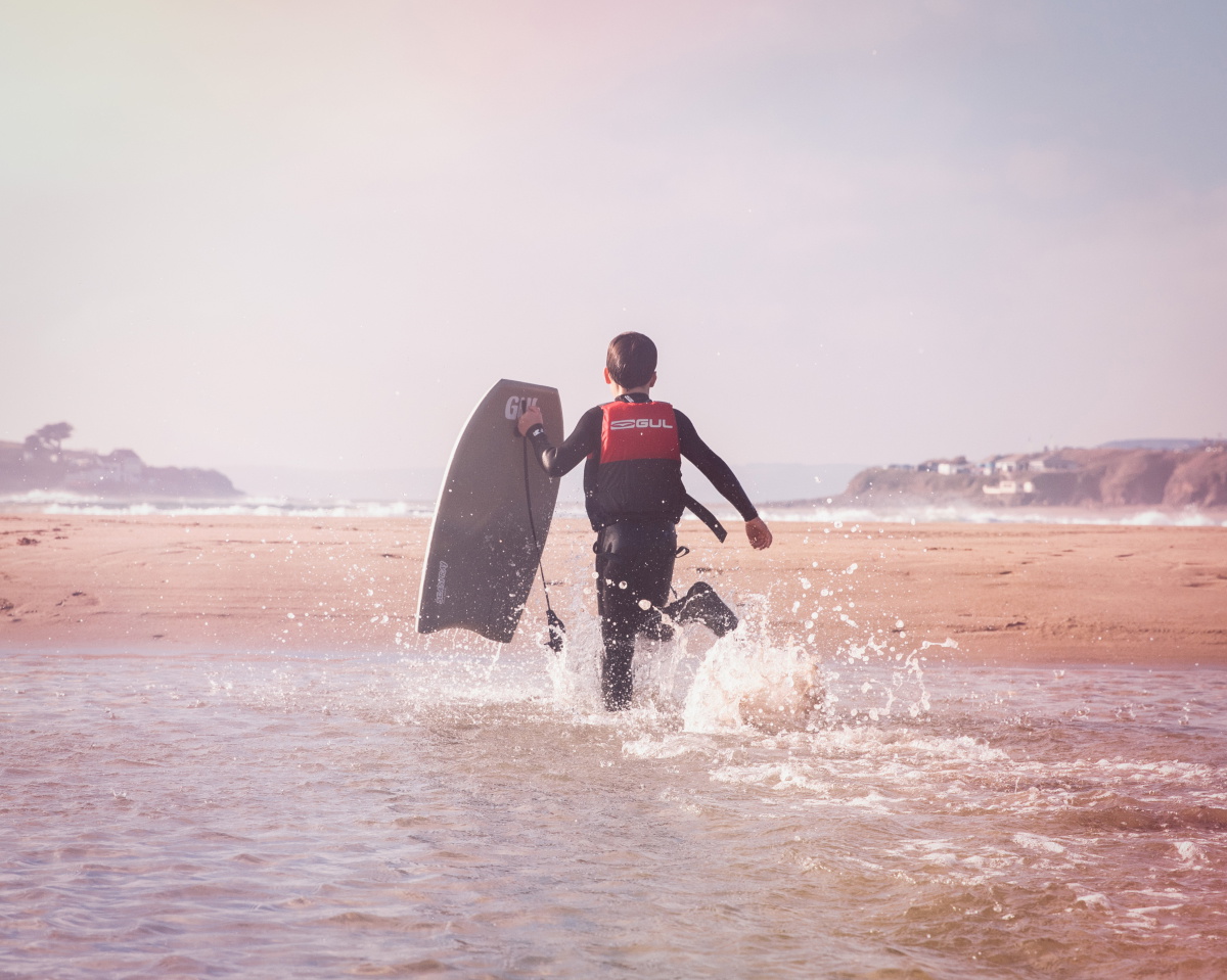 Child running towards the ocean with Gul body board